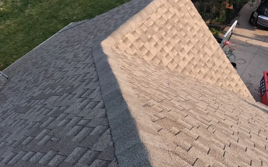 Aerial view of a completed asphalt shingle roof hip line, photographed from directly above with a driveway and work truck visible below.